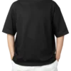 A man wearing a black oversized t-shirt and white shorts, with his hands in his pockets. Product image for an oversized black t-shirt.
