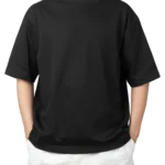 A man wearing a black oversized t-shirt and white shorts, with his hands in his pockets. Product image for an oversized black t-shirt.