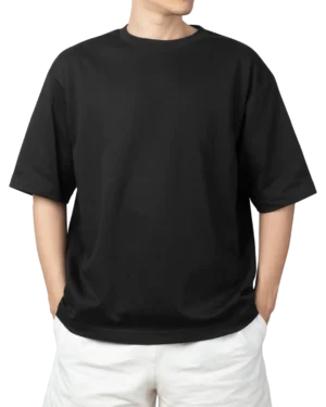 A man wearing a black oversized t-shirt and white shorts, with his hands in his pockets. Product image for an oversized black t-shirt.