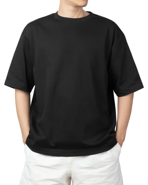 A man wearing a black oversized t-shirt and white shorts, with his hands in his pockets. Product image for an oversized black t-shirt.