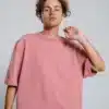 A young man with curly hair looking up, wearing a dusty pink oversized t-shirt. Casual and stylish product shot.