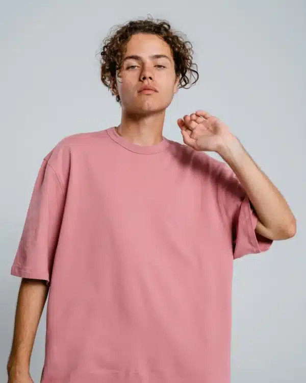 A young man with curly hair looking up, wearing a dusty pink oversized t-shirt. Casual and stylish product shot.